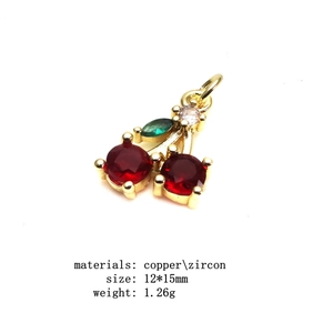 Macro view of gold copper cherry pendant with red zircon stones and green leaf detail