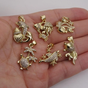 Gold plated ocean themed charms with micro paved cubic zirconia held in hand for size