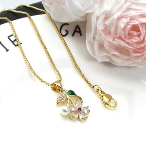 Macro shot of gold plated necklace with zircon flower, green leaf, and white pearl