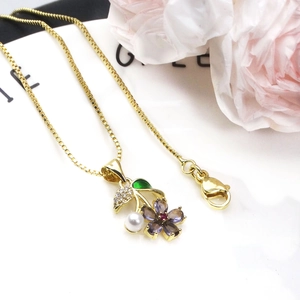 Macro detail of gold flower pendant with purple stones, white pearl and green enamel leaf