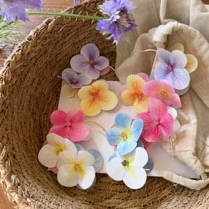Colorful and vibrant floral C-shaped hoop earrings presented in a rustic woven basket