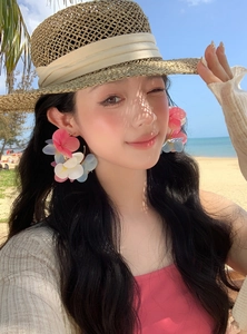 Close-up view of an Asian model wearing colorful dopamine flower C-shaped earrings on a beach