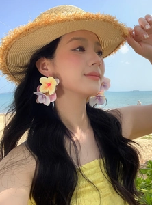 Close-up of model wearing vibrant oversized floral C-shaped earrings on a sunny beach