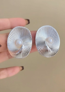 Primo piano di orecchini a spirale retrò in argento con perle centrali tenuti in mano