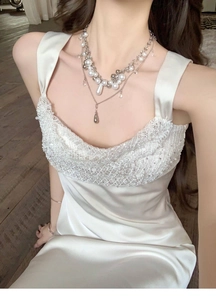 Elegant layered pearl necklace with silver pendants on a white lace satin dress detail.
