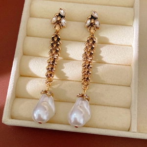 Detailed close-up of vintage golden wheatear earrings with rhinestones and baroque pearls