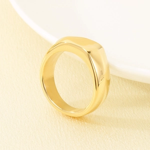 Nahaufnahme eines fein polierten Siegelrings aus goldfarbenem Edelstahl auf hellem Stoff.