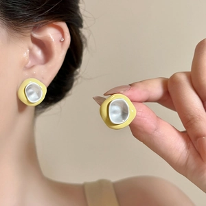 Detail of irregular yellow drip oil stud earrings worn on ear and held in hand.