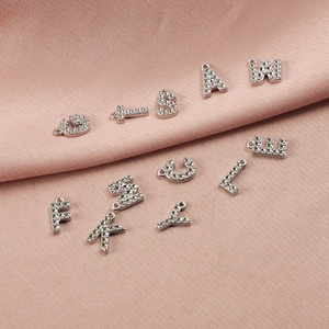 Détail de breloques lettres en argent serties de strass sur tissu rose