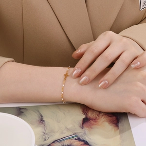 Vue rapprochée d'un élégant bracelet croix en acier inoxydable doré avec perles blanches au poignet