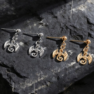Détail macro de boucles d'oreilles dragon gothiques en argent et or sur fond de pierre