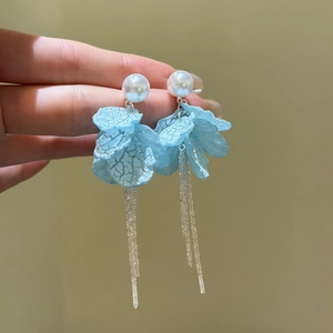 Close-up of light blue petal earrings with pearl studs and silver tassel chains.