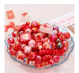 Macro shot of red acrylic DIY beads featuring hearts, stars and mahjong motifs in a glass bowl