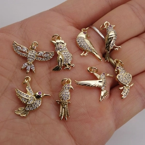 Golden bird charms with zircons for DIY necklaces and bracelets displayed on a hand