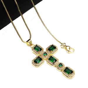 Detailed macro view of a gold cross pendant with emerald stones and zircon accents