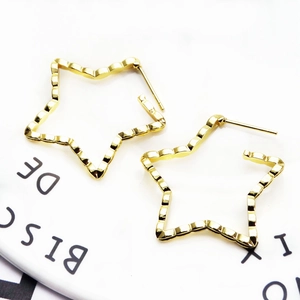 Macro shot of gold star-shaped earrings with textured wavy metal surface on a white page