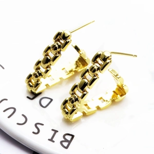 Macro view of gold C-shaped chain link earrings with polished finish on white surface