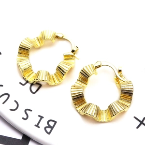Macro detail of golden geometric C-shaped hoop earrings with a textured wavy ruffled finish