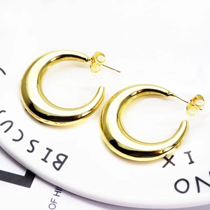 Detailed view of chunky golden C-shaped hoop earrings on a decorative white plate