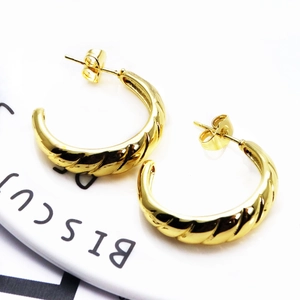Detailed view of gold C-shaped earrings with spiral twisted metal texture and wave reflections