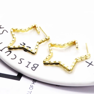 Close-up of golden star-shaped earrings with unique wavy metal texture on a ceramic plate