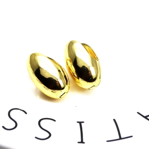 Macro shot of polished 18K gold plated teardrop earrings on a white ceramic tray