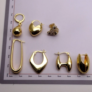 Various 18K gold-plated earrings with pearls on a measurement board for size comparison