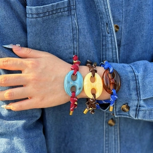 Dettaglio di tre bracciali colorati regolabili con maglie in acrilico indossati al polso.