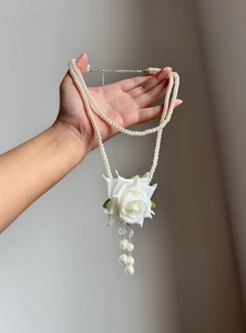 Close-up of elegant double-layer pearl necklace with white rose pendant and tassel detail.
