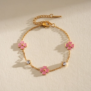 Detalle de una pulsera de acero inoxidable dorada con flores rosas y circonitas