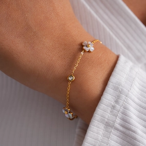 Detalle de una pulsera de acero dorado con flores de nácar y circón brillante