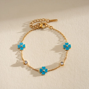 Detalle de pulsera de acero dorado con flores de esmalte azul y detalles de circón.