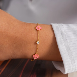 Vista macro detallada de una pulsera de acero inoxidable dorada con flores rosas y circón.