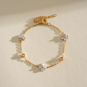 Elegante pulsera de acero inoxidable dorado con flores de nácar y piedras claras.