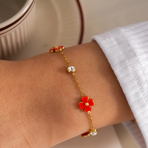 Primer plano de una pulsera elegante de acero dorado con flores rojas y circonitas