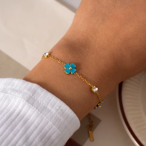 Detalle de una pulsera de acero inoxidable dorado con dije de flor azul y circonitas