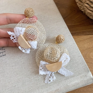 Détail de boucles d'oreilles chapeau de soleil en raphia avec nœud en dentelle