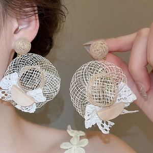 Vue détaillée de boucles d'oreilles chapeau de paille en raphia et nœud en dentelle.