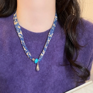 Dettaglio di una collana a foulard floreale blu con perla turchese e ciondolo a goccia.