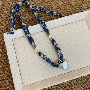 Dettaglio collana foulard floreale blu con ciondolo a cuore in argento su un vassoio