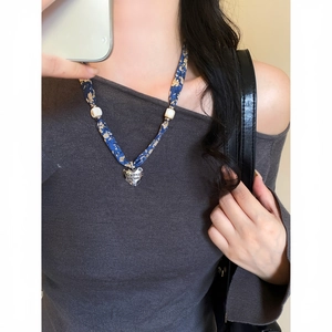Primo piano di una collana a foulard in seta floreale blu con ciondolo a cuore su modella.