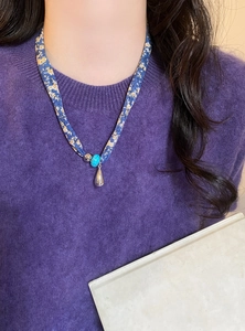 Primo piano della collana a sciarpa in seta floreale blu con pendente a goccia.