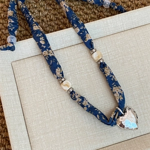 Dettaglio della collana foulard in seta a fiori blu con ciondolo a cuore martellato