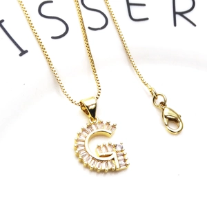 Detalle de collar con letra G dorada, incrustaciones de circón y cadena de caja