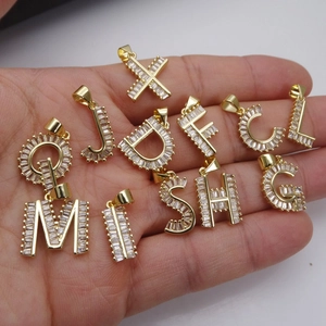 Colgantes de letras doradas con circonitas en la mano mostrando varios modelos de letras