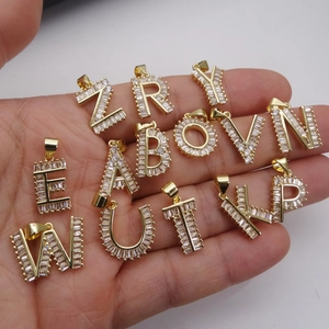 Colgantes de letras doradas con circonitas baguette, mostrados en la mano como referencia