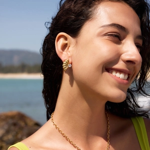 Vista di un orecchino a conchiglia dorato con zircone indossato da una modella sulla spiaggia