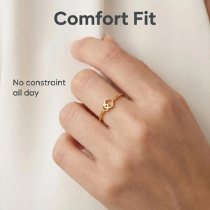 Nahaufnahme eines geometrischen Goldrings am Finger vor weißem Stoffhintergrund.