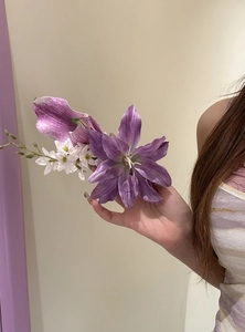 Detail of a large purple lily hair clip being held by a model with long hair.