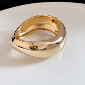 Statement chunky irregular gold metal bangle with glossy finish and minimalist design